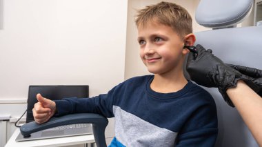 Küçük bir çocuk, sarışın bir genç, otolaringolojistin ofisinde oturuyor, doktorda kulak muayenesi yaptırıyor, endişeli, duygusal, ama gülümsüyor. Fiziksel muayene.