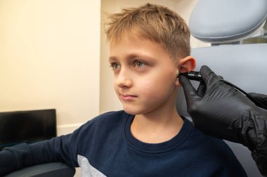 Küçük bir çocuk, sarışın bir genç, otolaringolojistin ofisinde oturuyor, doktorda kulak muayenesi yaptırıyor, endişeli, duygusal, ama gülümsüyor. Fiziksel muayene.