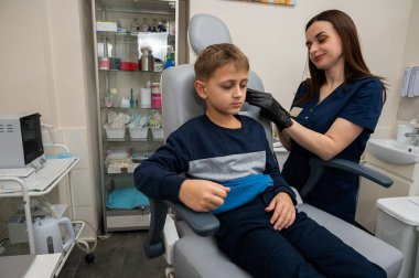 Küçük bir çocuk, sarışın bir genç, otolaringolojistin ofisinde oturuyor, doktorda kulak muayenesi yaptırıyor, endişeli, duygusal, ama gülümsüyor. Fiziksel muayene.