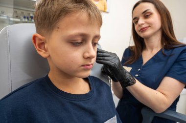 Küçük bir çocuk, sarışın bir genç, otolaringolojistin ofisinde oturuyor, doktorda kulak muayenesi yaptırıyor, endişeli, duygusal, ama gülümsüyor. Fiziksel muayene.