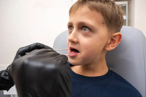 throat examination, little boy, fair-haired teenager, sitting in otolaryngologist\'s office, doctor examines throat, worried, emotional, but smiling. Physical examination