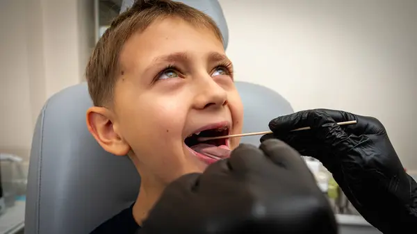 little boy, fair-haired teenager, sitting in otolaryngologist\'s office, being examined, throat swab, test by doctor, emotional but smiling. Physical examination
