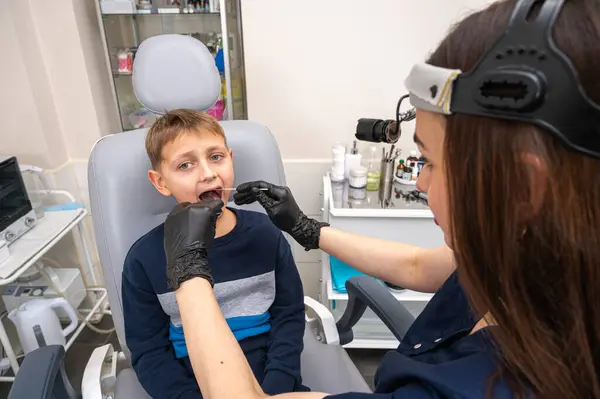little boy, fair-haired teenager, sitting in otolaryngologist\'s office, being examined, throat swab, test by doctor, emotional but smiling. Physical examination