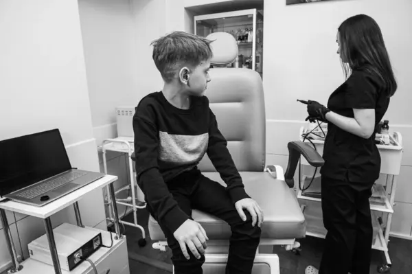 black and white photo, throat examination, little boy, fair-haired teenager, sitting in otolaryngologist\'s office, doctor examines throat, worried, emotional, but smiling. Physical examination