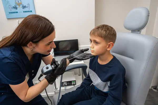 throat examination, little boy, fair-haired teenager, sitting in otolaryngologist's office, doctor examines throat, worried, emotional, but smiling. Physical examination