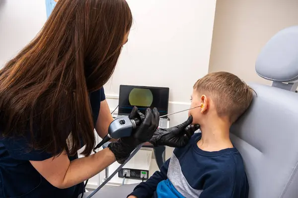 little boy, fair-haired teenager, sitting in an otolaryngologist\'s office, having an ear examination at the doctor\'s, worried, emotional, but smiling. Physical examination