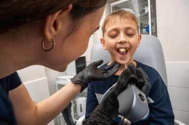 Boğaz muayenesi, küçük bir çocuk, sarışın bir genç, otolaringolojistin ofisinde oturuyor, doktor boğazını inceliyor, endişeli, duygusal, ama gülümsüyor. Fiziksel muayene.