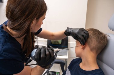 Küçük bir çocuk, sarışın bir genç, otolaringolojistin ofisinde oturuyor, doktorda kulak muayenesi yaptırıyor, endişeli, duygusal, ama gülümsüyor. Fiziksel muayene.