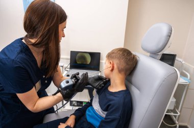 Küçük bir çocuk, sarışın bir genç, otolaringolojistin ofisinde oturuyor, doktorda kulak muayenesi yaptırıyor, endişeli, duygusal, ama gülümsüyor. Fiziksel muayene.