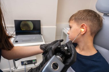 Küçük bir çocuk, sarışın bir genç, otolaringolojistin ofisinde oturuyor, doktorda kulak muayenesi yaptırıyor, endişeli, duygusal, ama gülümsüyor. Fiziksel muayene.