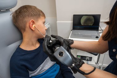 Küçük bir çocuk, sarışın bir genç, otolaringolojistin ofisinde oturuyor, doktorda kulak muayenesi yaptırıyor, endişeli, duygusal, ama gülümsüyor. Fiziksel muayene.