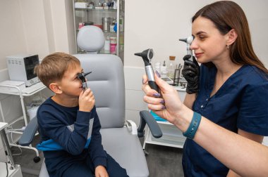 Küçük bir çocuk, sarışın bir genç, otolaryngolojistin ofisinde, doktorun kulak muayenesinde, doktorla oynuyor, duygusal ama gülümseyen, rol yapan. Fiziksel muayene.