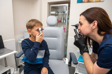 Küçük bir çocuk, sarışın bir genç, otolaryngolojistin ofisinde, doktorun kulak muayenesinde, doktorla oynuyor, duygusal ama gülümseyen, rol yapan. Fiziksel muayene.