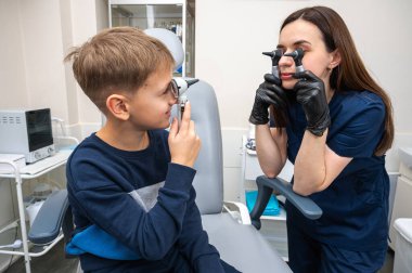 Küçük bir çocuk, sarışın bir genç, otolaryngolojistin ofisinde, doktorun kulak muayenesinde, doktorla oynuyor, duygusal ama gülümseyen, rol yapan. Fiziksel muayene.