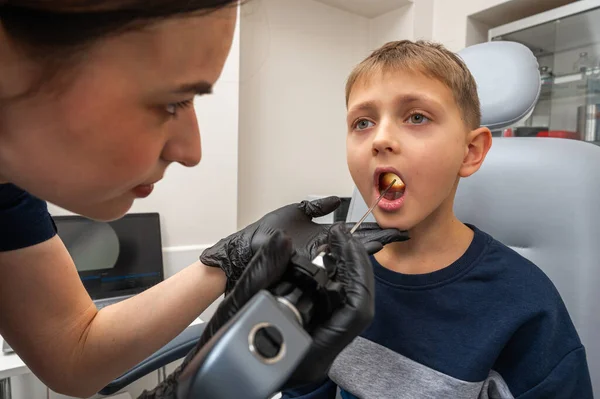 throat examination, little boy, fair-haired teenager, sitting in otolaryngologist\'s office, doctor examines throat, worried, emotional, but smiling. Physical examination