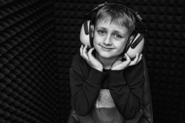 siyah ve beyaz portre, gülümseyen sarı saçlı, kulaklıklı genç çocuk, karanlık odada sese karşı bakıyor. Karanlık bir odada. İşitme testi, sesler
