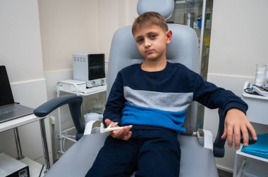 Küçük duygusal çocuk, sarışın ergen, otolaringolojistin ofisinde oturuyor, muayene için doktoru bekliyor, ama gülümsüyor. Fiziksel muayene.
