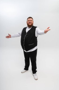 Beyaz tişörtlü ve yelekli sakallı bir adamın duygusal portresi. Hafif arka planda, kollarını yanlara, duygulara, yazmak için bir yer.