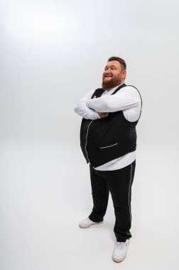 Beyaz arka planda siyah yelek ve açık tişörtlü mutlu sakallı bir adamın duygusal portresi. Stüdyo çekimi. Duygular, yazacak bir yer.