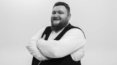 Beyaz tişörtlü, beyaz yelekli, sakallı bir adamın siyah ve beyaz duygusal portresi. Arka planda hafif bir arka plan, öğle yemeği, duygular, yazıtlar için yer.