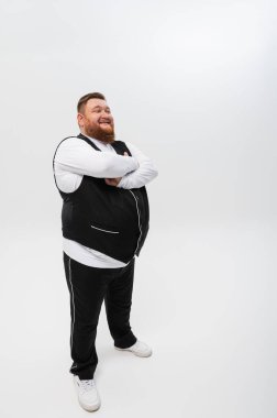 Beyaz arka planda siyah yelek ve açık tişörtlü mutlu sakallı bir adamın duygusal portresi. Stüdyo çekimi. Duygular, yazacak bir yer.