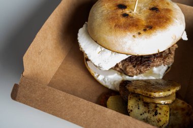 Et pirzolalı hamburger, hafif bir arka planda el işi paketinde süzme peynir.