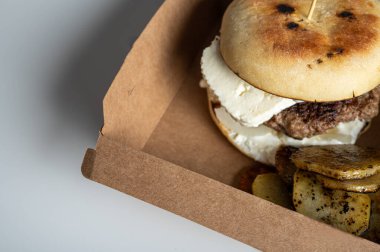 Et pirzolalı hamburger, hafif bir arka planda el işi paketinde süzme peynir.