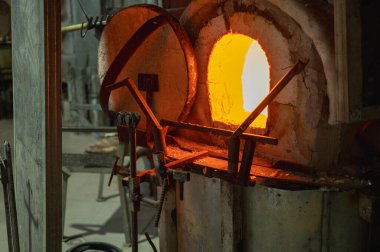 Bir atölyede yoğun ateş altında sıcak erimiş cam oluşturan cam üfleyicisinin yakın plan görüntüsü, patlama fırını. Camların içindeki ustalar tarafından elle işleniyor. Seçici odak