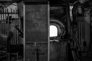 Siyah ve beyaz fotoğraf, cam üfleyicinin yakın çekim görüntüsü atölyede yoğun ateş altında erimiş cam oluşumu, patlama fırını. Camların içindeki ustalar tarafından elle işleniyor. Seçici odak