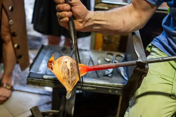 stock image Close-up of a glassblower shaping hot molten glass under a high fire in a workshop. Manual processing of glass by masters inside the glass. Selective focus