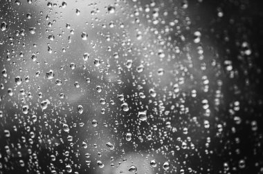siyah ve beyaz fotoğraf, cam üzerindeki yağmur damlalarının arka planı, güneş ışığıyla bulutlu bir gün, seçici odak