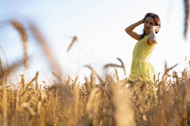 Güzel genç kız buğday tarlasında duruyor, sırtüstü bakıyor gülümsüyor, sarı Vog elbiseler giyiyor, yazı için yer, tarlalar ve Ukrayna 'nın doğası.
