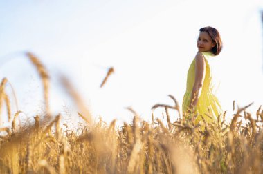 Güzel genç kız buğday tarlasında duruyor, sırtüstü bakıyor gülümsüyor, sarı Vog elbiseler giyiyor, yazı için yer, tarlalar ve Ukrayna 'nın doğası.