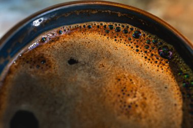 Kahve bardakta, yakın plan köpüklü, ahşap bir masa, arka plan, sabah ışığı ışınları, üst görüş, yazma yeri, seçici odaklanma.