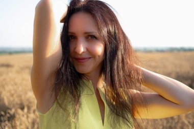 Buğday tarlasında güzel, genç, duygusal bir kız batan güneşin ışınlarında sarı bir elbise, arka plan ışığı, gün batımı, gülümseme, tarlalar ve Ukrayna 'nın doğası.