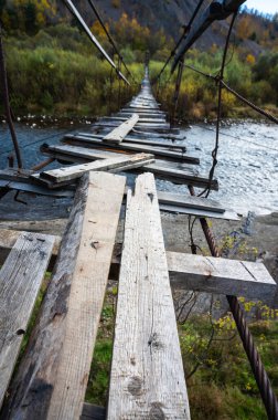 Eski, yıkık asma köprüsü nehir boyunca uzanıyor, macera ve tehlike hissi yaratıyor. Kötüleşen ahşap kalaslar kırsal ve manzaralı bir bölgeye risk ve gizem atmosferi ekler.