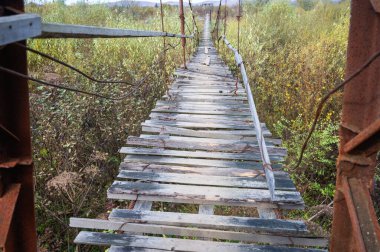 Eski, yıkık asma köprüsü nehir boyunca uzanıyor, macera ve tehlike hissi yaratıyor. Kötüleşen ahşap kalaslar kırsal ve manzaralı bir bölgeye risk ve gizem atmosferi ekler.
