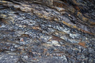 Farklı dokulara ve doğal renk tonlarına sahip katmanlı tortul kaya oluşumlarına yakın çekim. Jeoloji, doğa ve soyut arka planlar için mükemmel. Eski taş katmanlarının engebeli ve yıpranmış detaylarını yakalar.