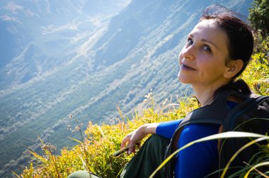 Sırt çantalı dağlarda parlak yapraklarla çevrili yemyeşil ormanda doğa yürüyüşünden zevk alan gülümseyen bir kadın. Açık hava macerası ve doğal çevrede sükunet, dağlar.