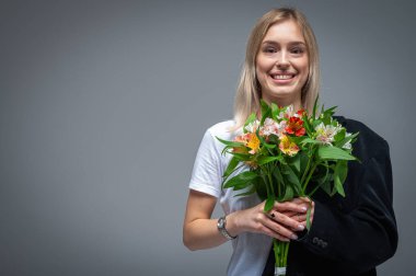 Bir buket taze çiçekle genç bir kadının portresi, ciddi görünüyor. Yumuşak ışıklandırma ve nötr arkaplan ile stüdyo çekimi, duyguları ve doğal güzelliği yakalamak