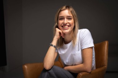 Kahverengi bir sandalyede oturan yorgun, bitkin genç kız beyaz bir tişört giyiyor, stres, endişe, yüzüne yakın eller. Bir iş ya da hayat temasının modern minimalist portresi, bir yazıt için yer