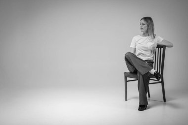 siyah ve beyaz fotoğraf, genç, duygusal, iş kadını deri bir sandalyede oturan, beyaz tişört giyen, stres, endişeler, dosdoğru ileriye bakan. Modern minimalist iş portresi ya da hayat.