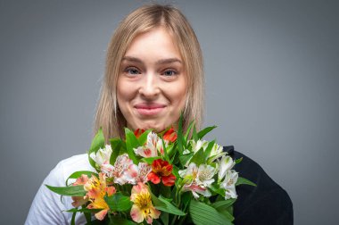 Bir buket taze bahar çiçeğiyle gülümseyen ve heyecanlı genç, duygusal bir kızın portresi. Yumuşak ışıklandırmalı stüdyo çekimi ve duyguları ve doğal güzelliği aktaran nötr bir arka plan.