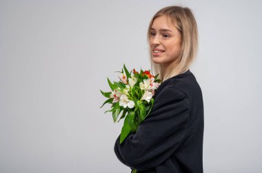 Bir buket taze bahar çiçeğiyle genç ve duygusal bir kızın portresi, gülümseyen ve heyecanlı, kenar manzaralı. Yumuşak ışıklandırma ve doğal güzelliği yansıtan nötr arkaplan ile stüdyo çekimi