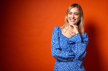 Düşünceli, duygusal, mavi elbiseli, çiçekli, turuncu arka planda bir kız. Yüz ifadesi, modern moda ve kendine güvenen duruş, duygular, jestler, yaşam tarzı ve duygular, yazıtlar için yer