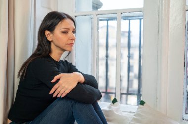 Düşünceli, üzgün kız rahat bir yatakta pencerenin kenarında oturuyor, yağmurlu bir günde sokağa bakıyor, aile sorunları yaşıyor. Düşünceli ruh hali, yalnızlık, rahatlama, kendini düşünme, zihinsel sağlık konsepti