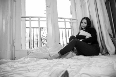 Siyah beyaz fotoğraf, düşünceli, üzgün kız pencerenin kenarında oturuyor, yağmurlu bir günde sokağa bakıyor, aile sorunları var. Düşünceli ruh hali, yalnızlık, rahatlama, zihinsel sağlık konsepti, seçici odaklanma