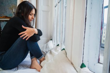 Düşünceli, üzgün kız rahat bir yatakta pencerenin kenarında oturuyor, yağmurlu bir günde sokağa bakıyor, aile sorunları yaşıyor. Düşünceli ruh hali, yalnızlık, rahatlama, kendini düşünme, zihinsel sağlık konsepti