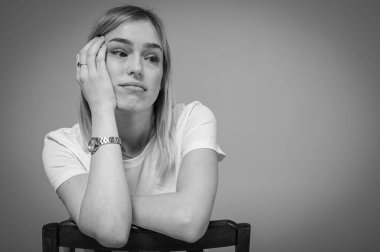 Siyah beyaz portre, yorgun, bitkin, stresli, kafası karışmış, sandalyeye yaslanmış, beyaz tişört giymiş genç bir kız. Modern portre, hayat teması, hayal kırıklığı, yazıtlar için