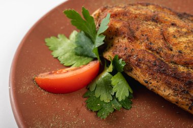 Taze maydanoz ve domates dilimleriyle süslenmiş, kıtır kıtır bir tabakta altın gevrek soslu ızgara tavuk göğsü. Sağlıklı yemek için mükemmel bir yüksek proteinli yemek.